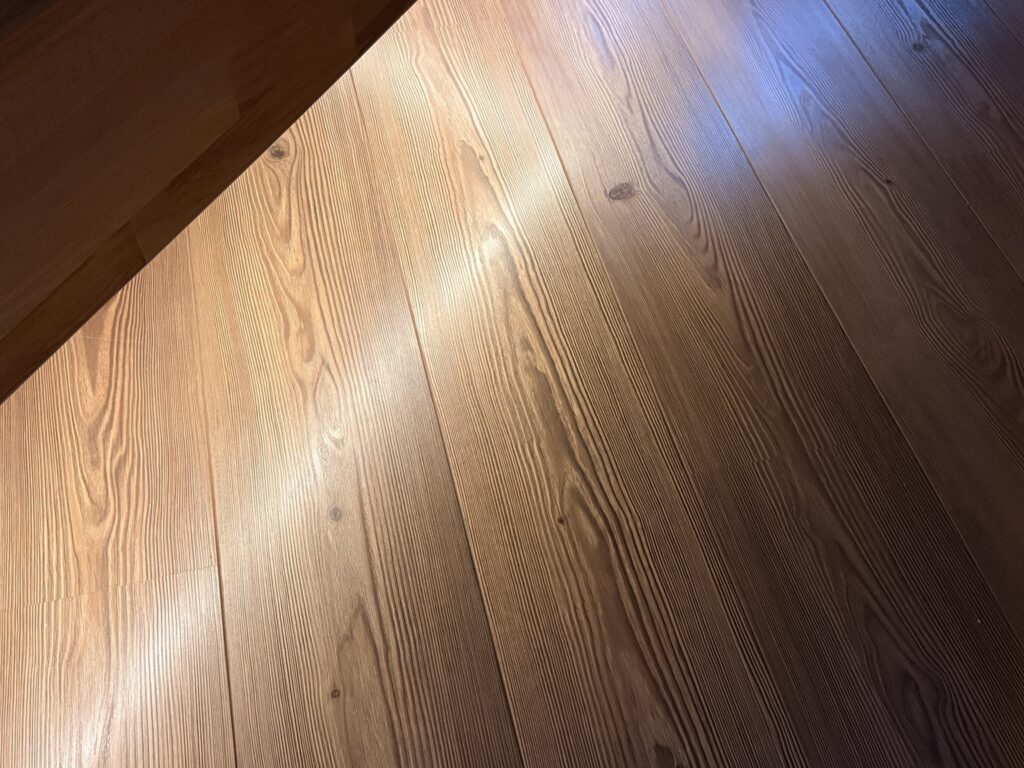 Holzboden im warmen Abendlicht mit dunkler Möbelkante und kühlem Licht im Hintergrund